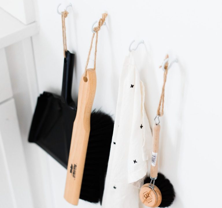 A dustpan, brush and cleaning tools hanging on hooks on a white wall
