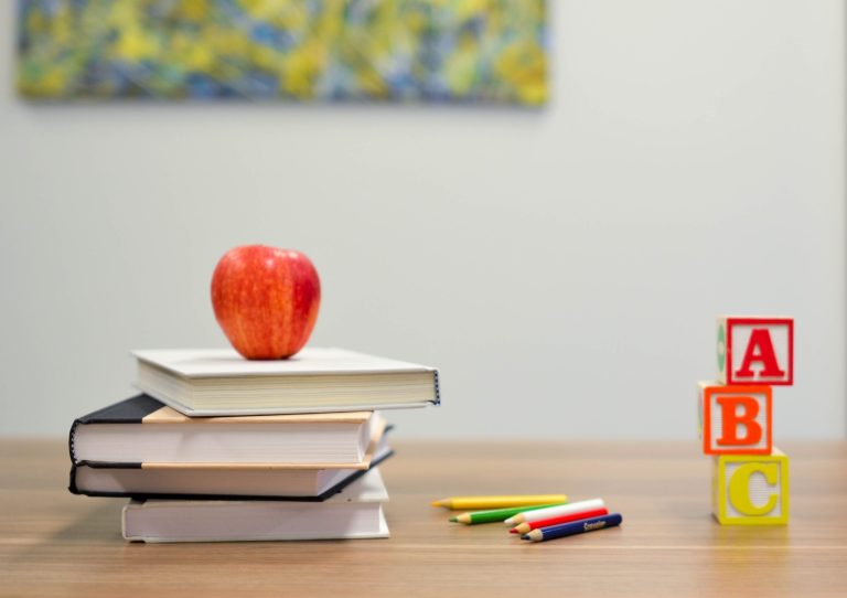 A stack of books with a red apple and ABC blocks on a desk