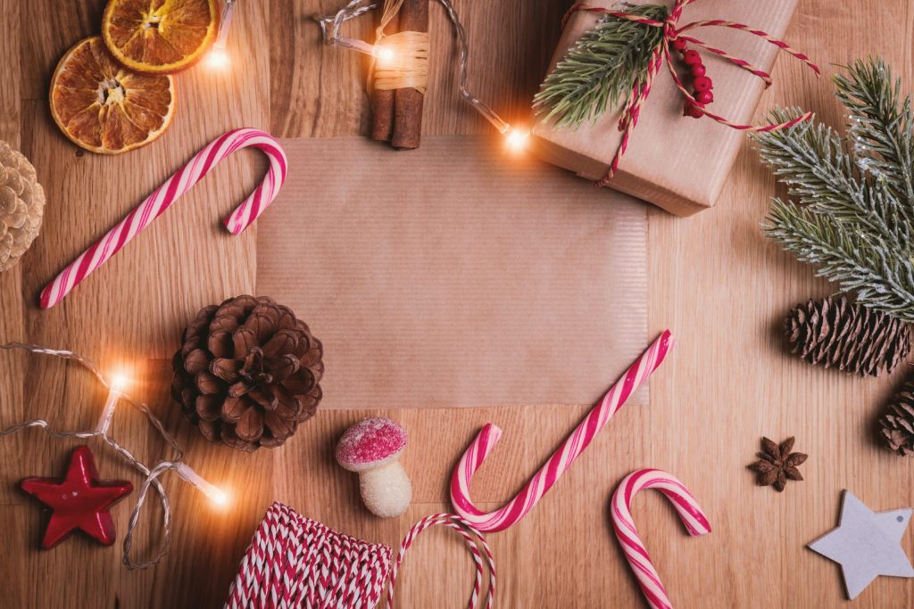 A Christmas flat lay with candy canes, dried oranges, pinecones and gifts on wood