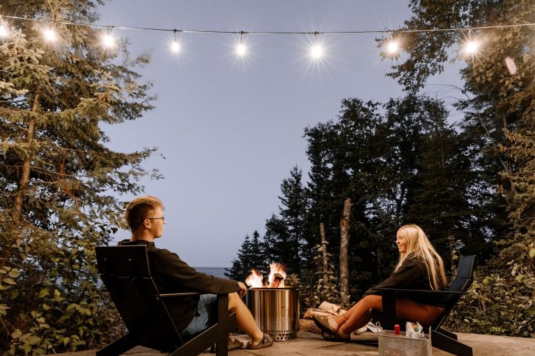 Two people relaxing by an outdoor fire pit at dusk