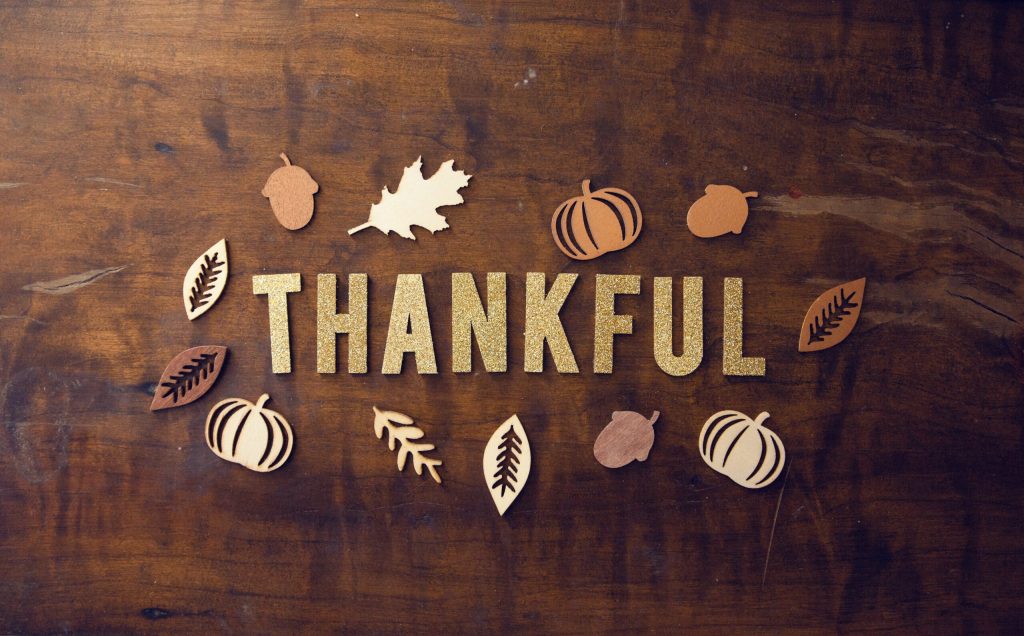 The word thankful spelled with autumn leaves and pumpkins on dark wood