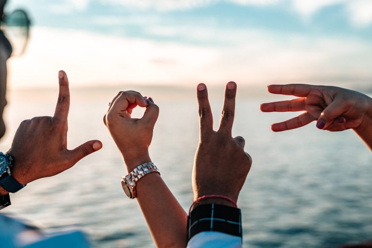Two people's hands spelling love against a sunset over water