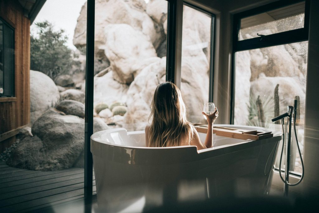 A woman relaxing in a freestanding bathtub with a view of desert rocks