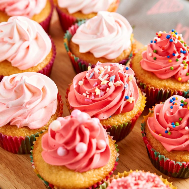 Pink-frosted cupcakes with sprinkles on a wooden table