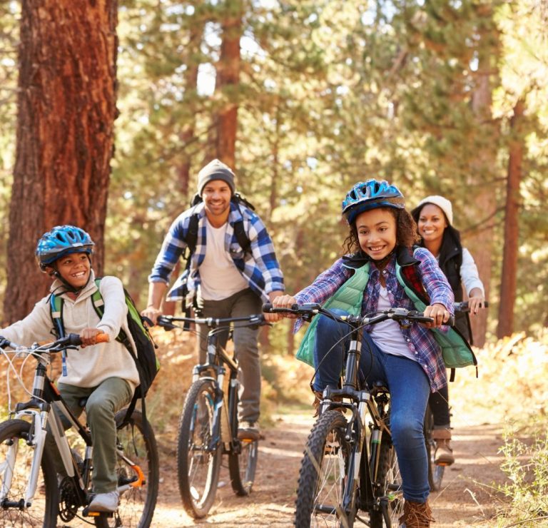 Family of four riding bikes on a forest trail in autumn